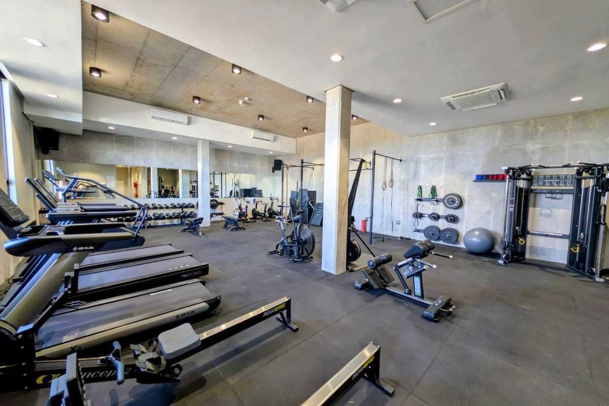 A well-equipped modern gym featuring rubberized flooring, mirrored walls, recessed lighting, and ducted air conditioning in a spacious, industrial-style setting.