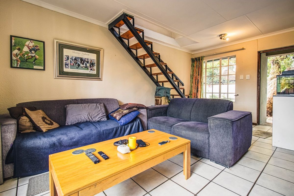 A living room featuring tiled flooring and an open-tread staircase leading to an upper level, with access to an exterior area.