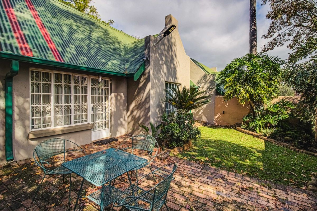 Rear view of the property featuring a brick-paved patio area, green corrugated metal roof, and established garden space.