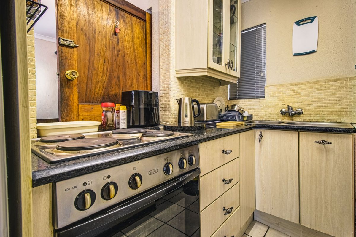A compact kitchen featuring built-in cabinetry, granite countertops, a Defy electric stove, and a tiled backsplash.