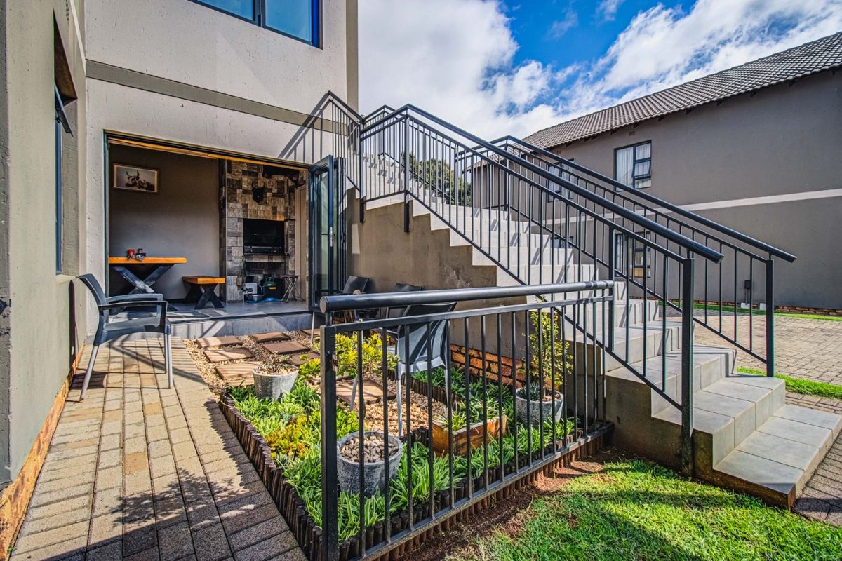 Rear exterior view featuring a paved patio, built-in braai area with stone cladding, and an external staircase with metal railings leading to the upper level.