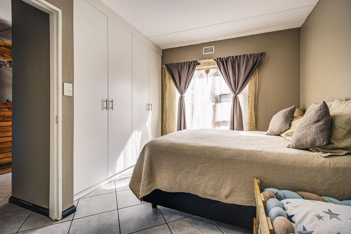A well-maintained bedroom featuring neutral wall tones, tiled flooring, and ample storage space provided by floor-to-ceiling built-in cupboards.