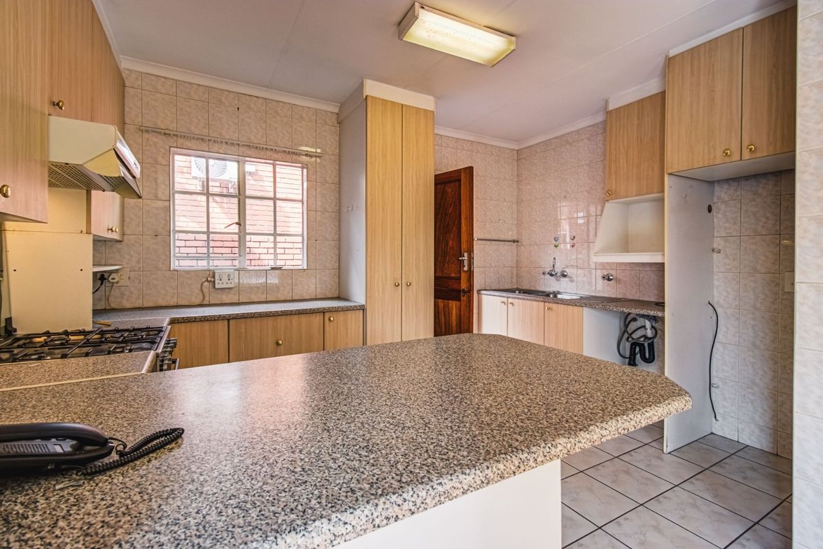 A functional kitchen featuring built-in cabinetry, laminate countertops, a gas hob with extractor, and tiled finishes throughout.