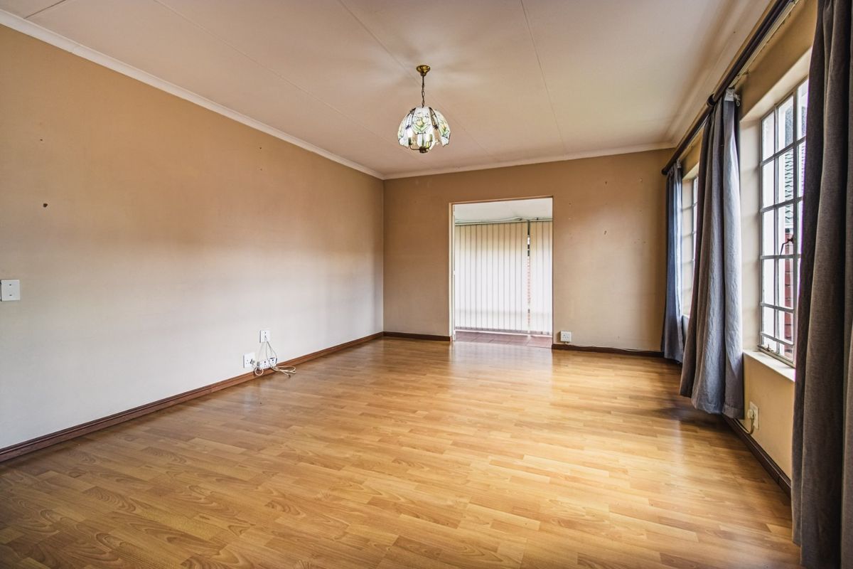A spacious, empty living room featuring laminate flooring, coved ceilings, and large windows, offering a neutral canvas for interior design.