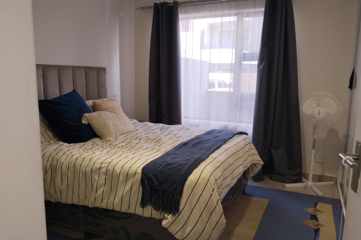 A functional bedroom featuring tiled flooring, a built-in headboard, and a window with curtain rails, providing a comfortable and practical living space.