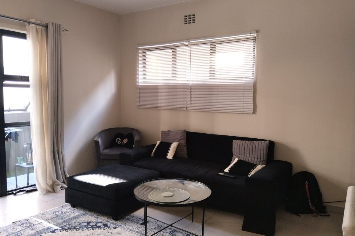 A well-lit living room featuring tiled flooring, a sliding glass door leading to an outdoor area, and fitted venetian blinds.