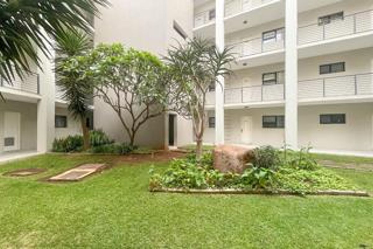 A well-maintained communal garden area featuring landscaped greenery and paved walkways, situated between the apartment building blocks with visible balconies.