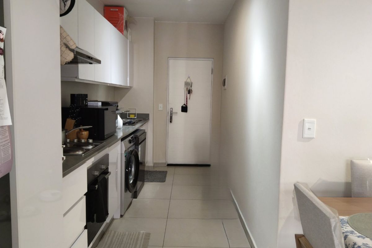 A compact, functional kitchen featuring white cabinetry, stainless steel appliances, and tiled flooring, leading directly to the apartment entrance.