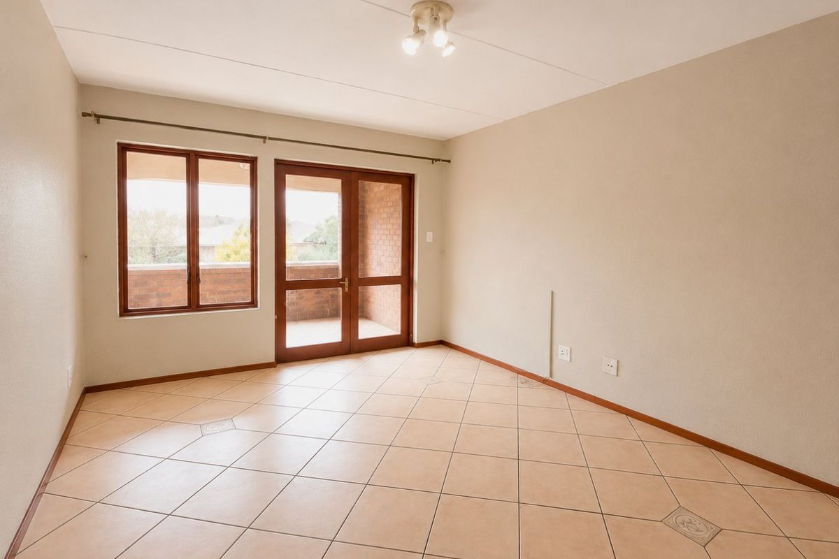 A bright, empty living room featuring neutral tiled flooring, a ceiling light fixture, and direct access to an outdoor balcony through glass-paneled doors.