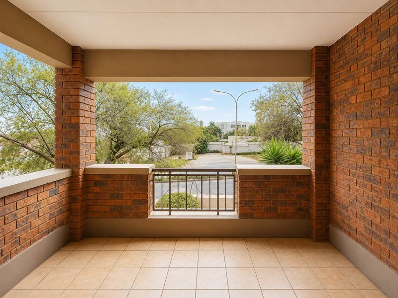 A covered balcony featuring exposed brick walls, tiled flooring, and a metal balustrade, offering an open view of the surrounding neighborhood.