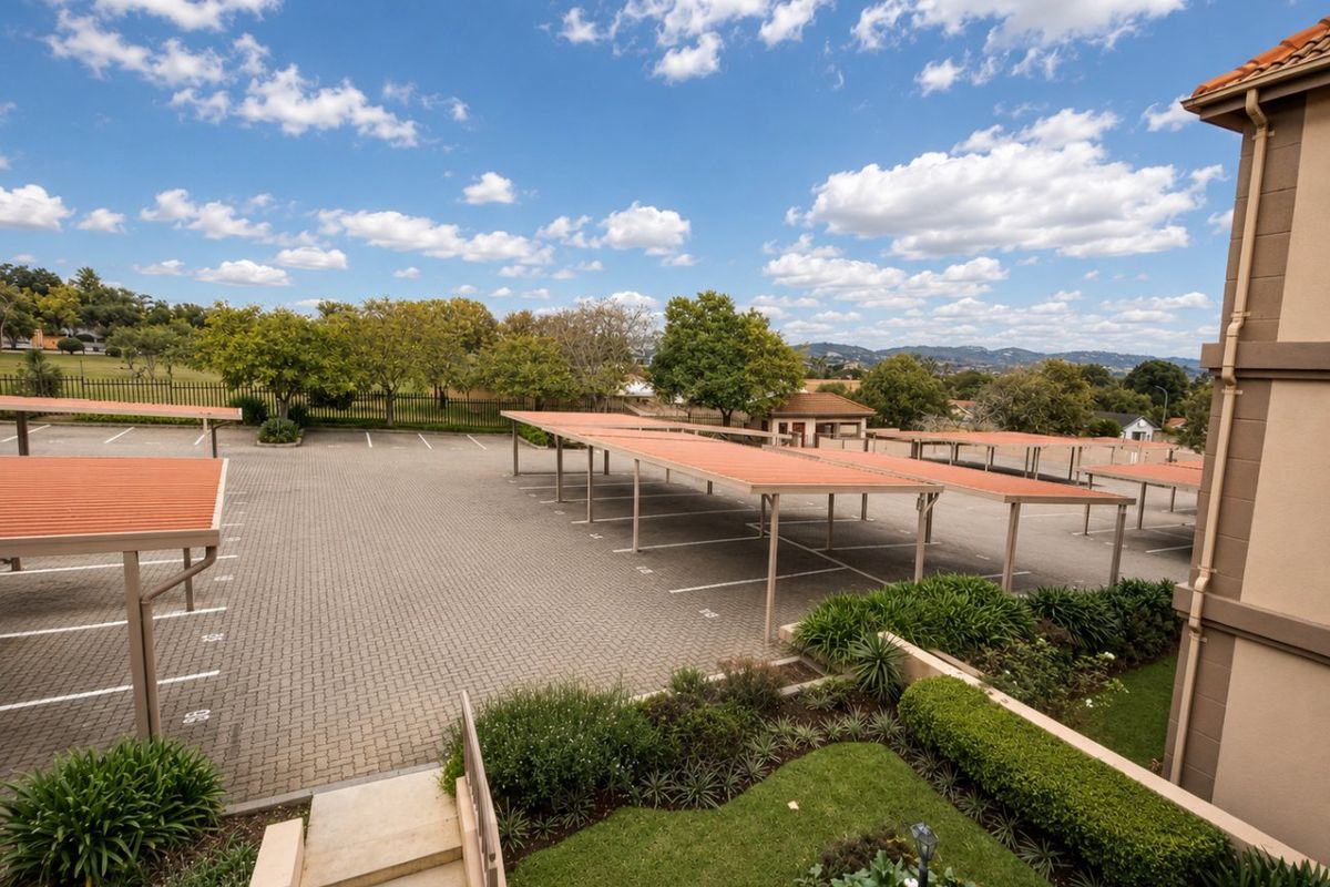 Elevated view of the apartment complex parking area featuring covered carports, paved driveway, and landscaped garden surrounds.