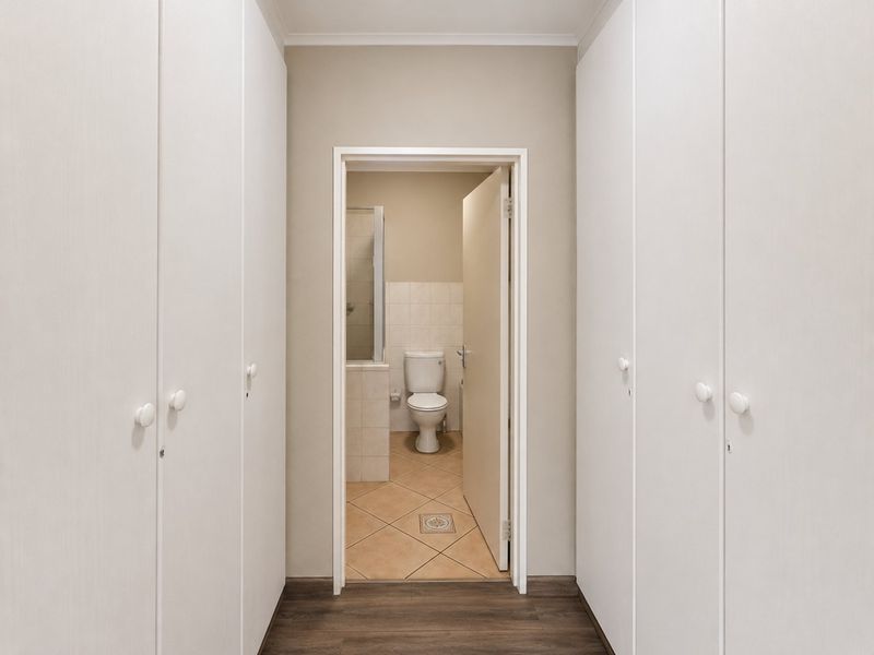 A hallway featuring extensive built-in floor-to-ceiling cabinetry leading into a tiled bathroom with a toilet and shower enclosure.
