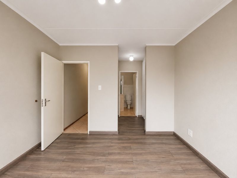 A clean, empty bedroom featuring neutral wall tones, modern wood-look laminate flooring, and direct access to an adjoining bathroom.