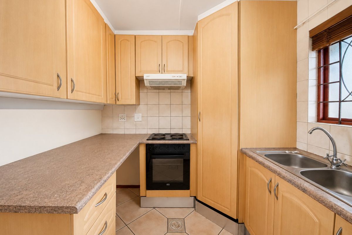 A functional kitchen featuring light wood cabinetry, laminate countertops, a built-in oven with hob, extractor fan, and a double stainless steel sink.