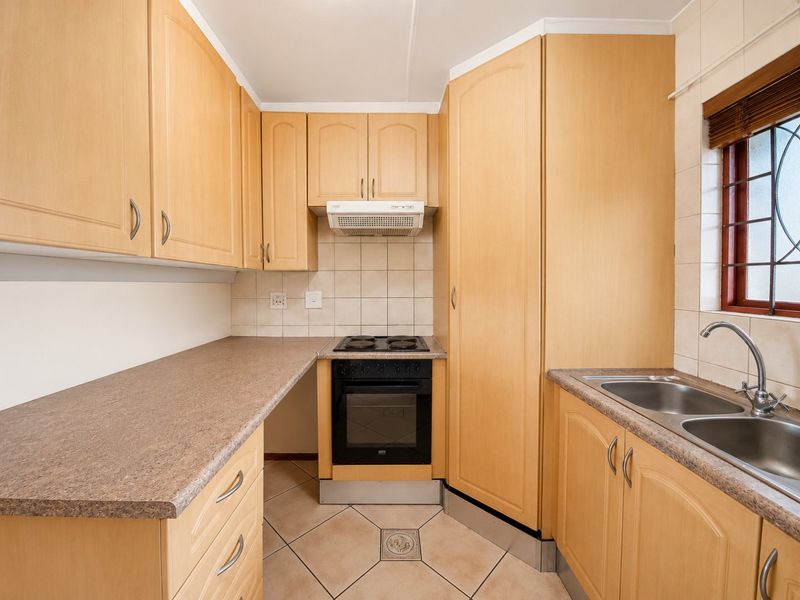 A functional kitchen featuring light wood cabinetry, laminate countertops, a built-in oven with hob, extractor fan, and a double stainless steel sink.