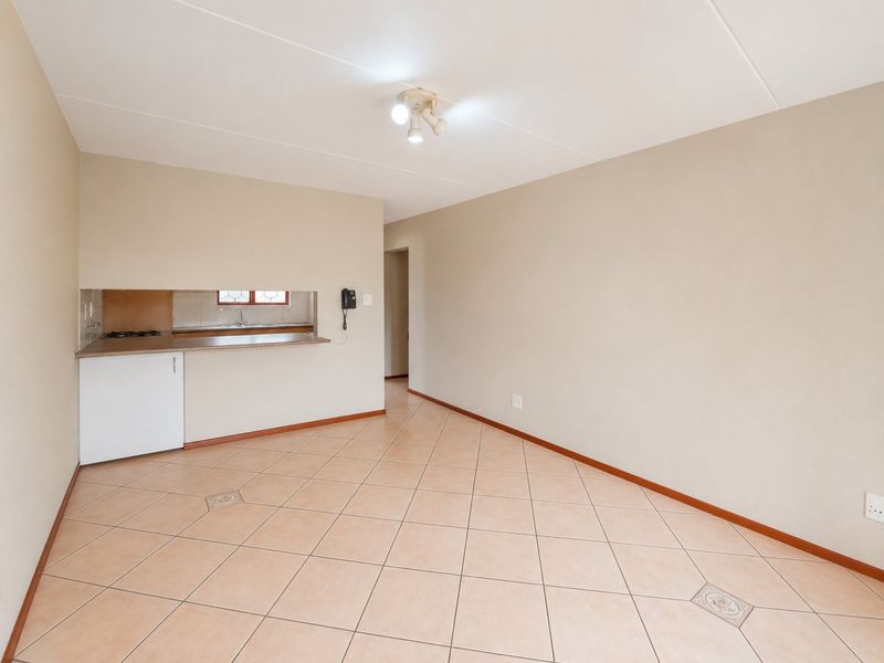 An open-plan living area featuring tiled flooring, a pass-through kitchen window, and neutral wall finishes, providing a functional and versatile space.