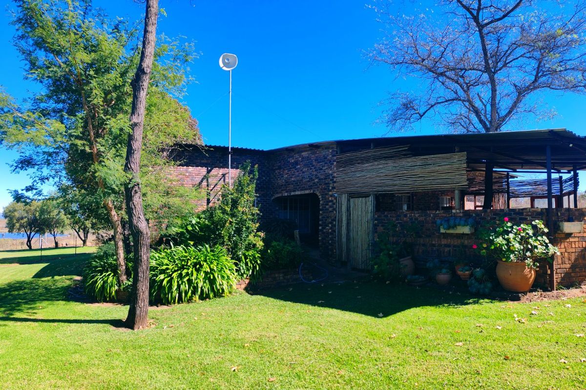 Rear view of a face brick farm dwelling featuring a covered patio area and expansive surrounding garden space.