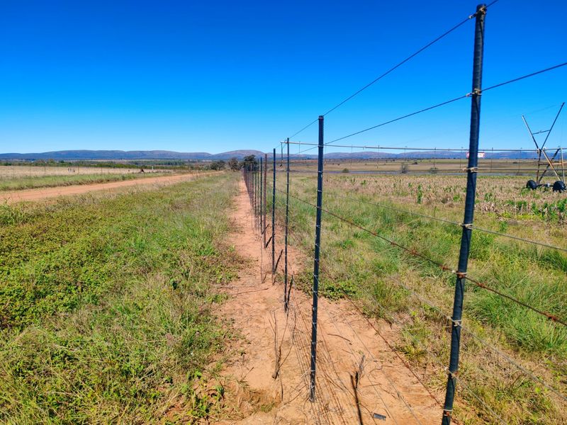 Expansive view of the farm landscape featuring wire perimeter fencing and agricultural irrigation infrastructure under a clear blue sky.