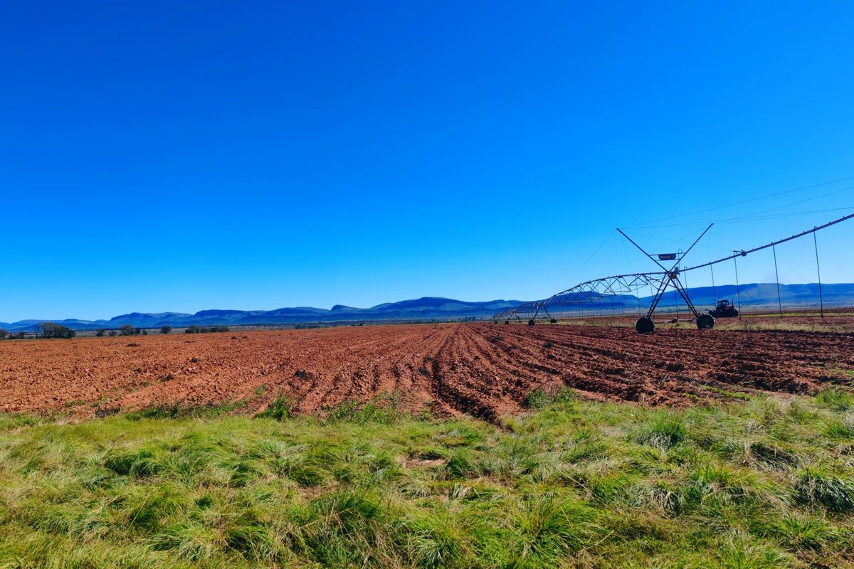 Expansive agricultural farmland featuring a center pivot irrigation system with scenic mountain views in the background.