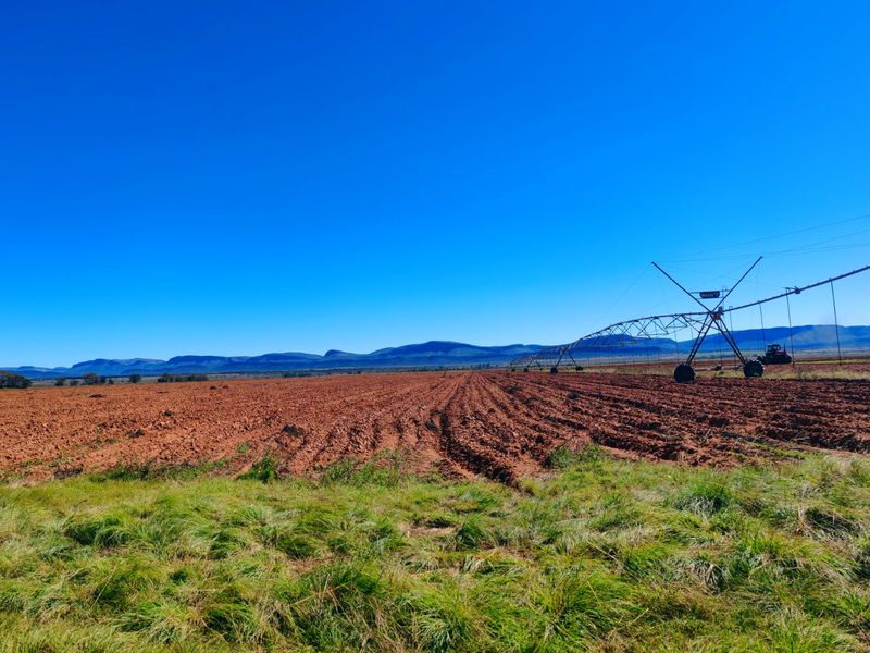 Expansive agricultural farmland featuring a center pivot irrigation system with scenic mountain views in the background.