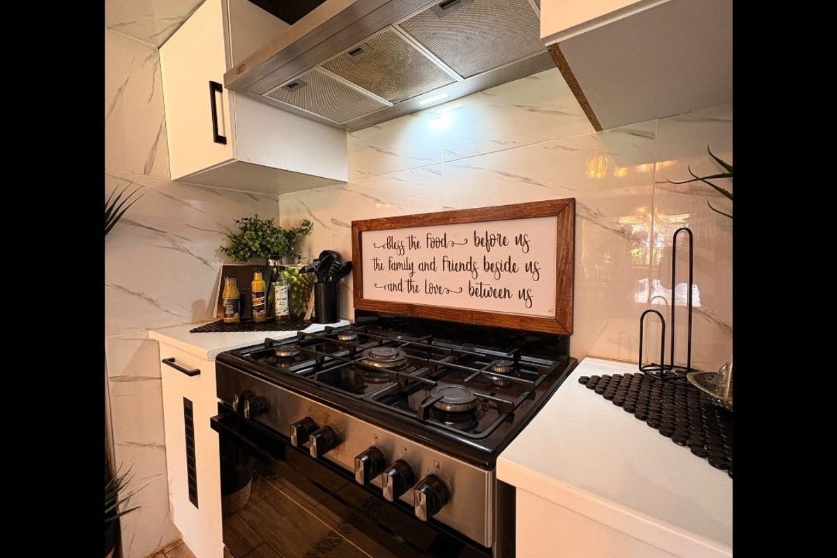 A modern kitchen featuring a stainless steel gas stove, integrated extractor fan, white cabinetry, and marble-effect wall tiling.