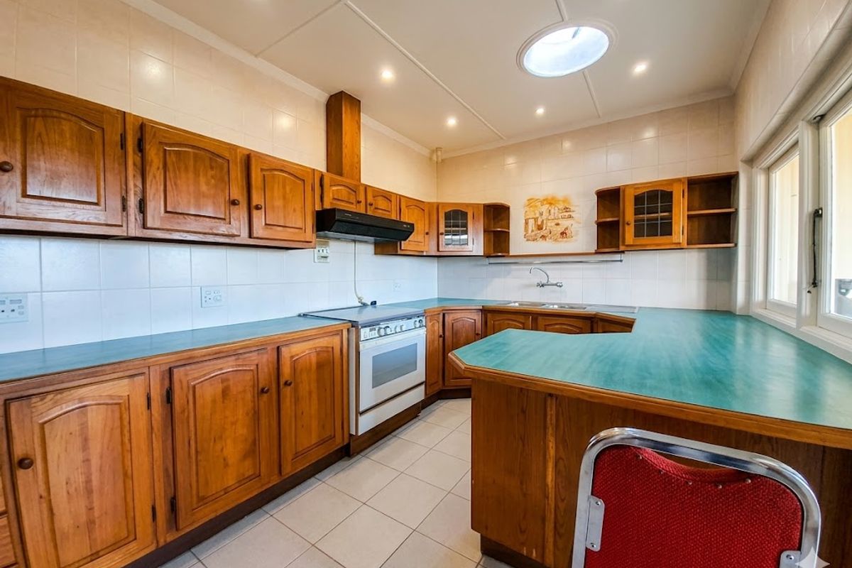 A functional kitchen featuring traditional wooden cabinetry, laminate countertops, a freestanding oven with extractor fan, and a bright skylight for natural illumination.