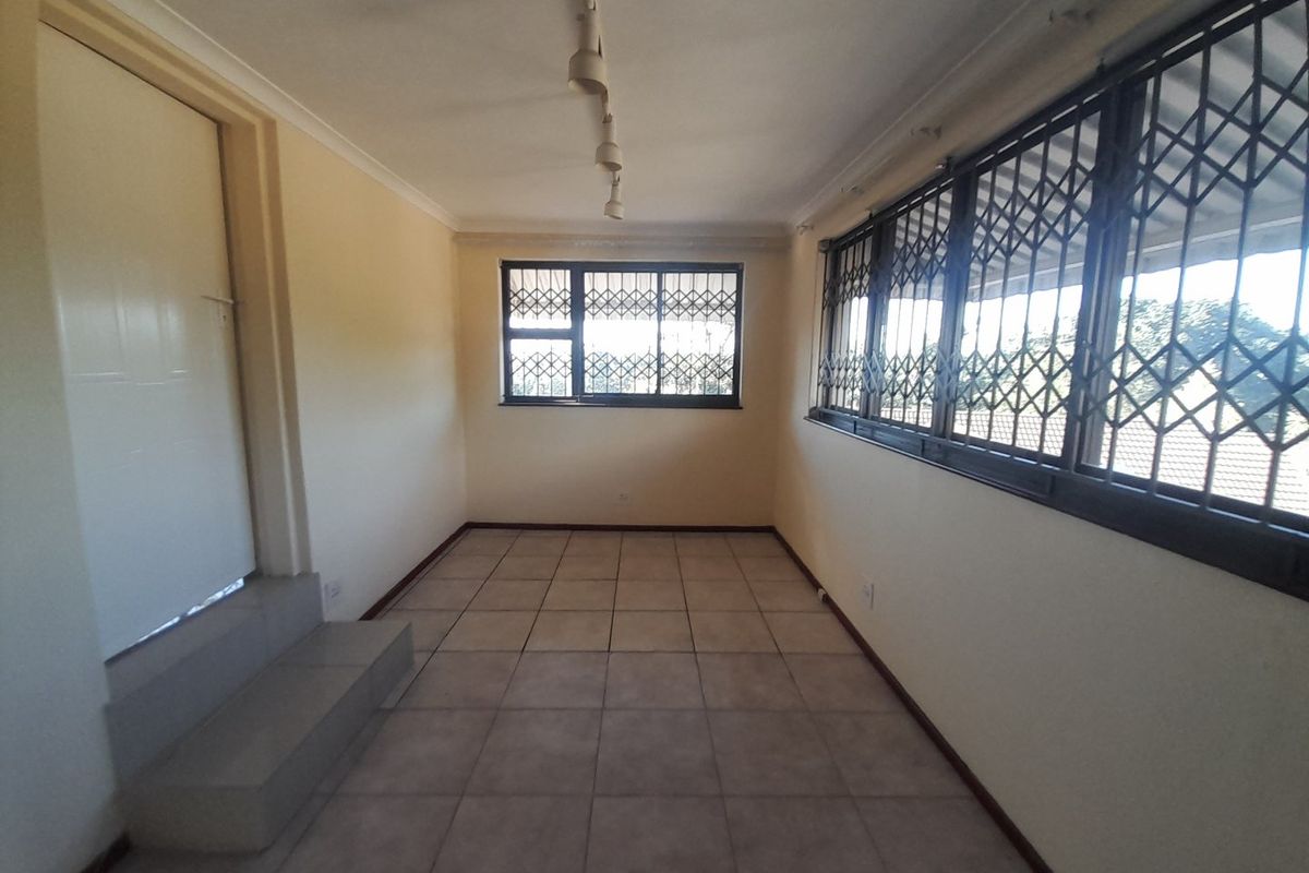 An empty, sunlit living area featuring neutral tiled flooring, coved ceilings, and secure window bars, offering a blank canvas for personalization.