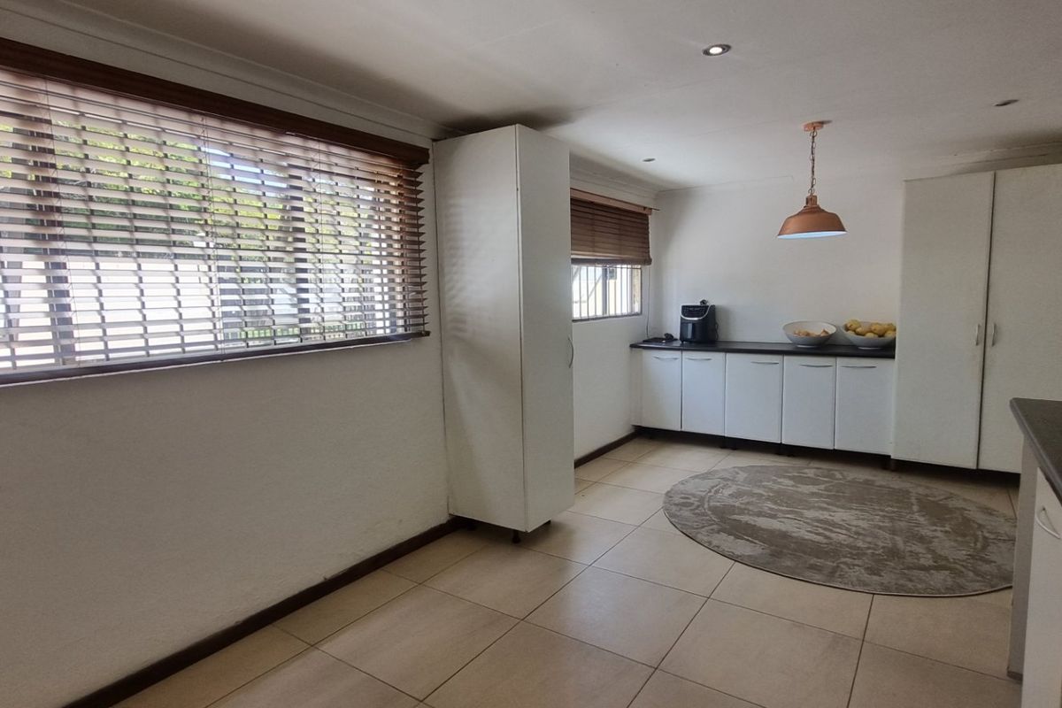 A functional kitchen area featuring tiled flooring, built-in cabinetry, and ample natural light provided by large windows with venetian blinds.