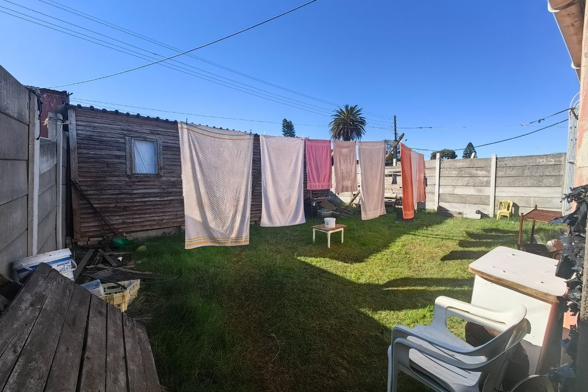Rear garden area featuring a lawn, precast concrete boundary walls, and a timber-clad outbuilding structure.