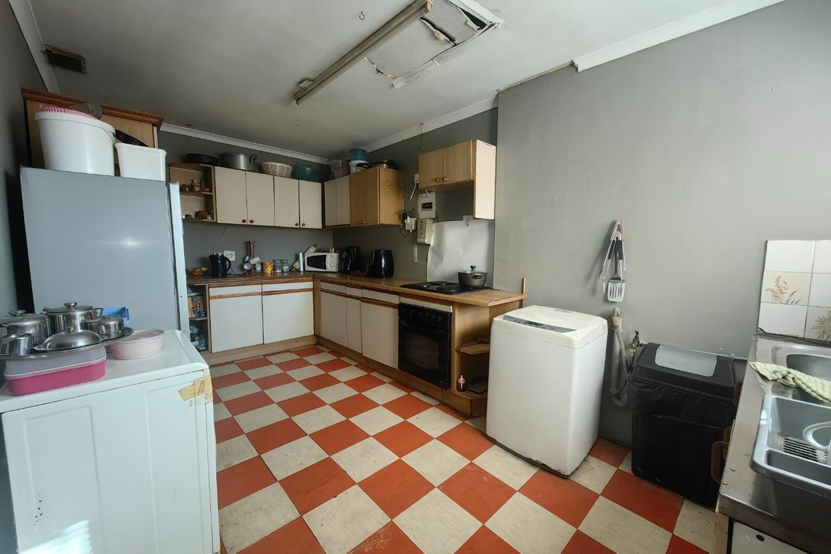 A dated kitchen featuring original cabinetry, laminate countertops, and a checkerboard vinyl floor, requiring modernization and ceiling repairs.