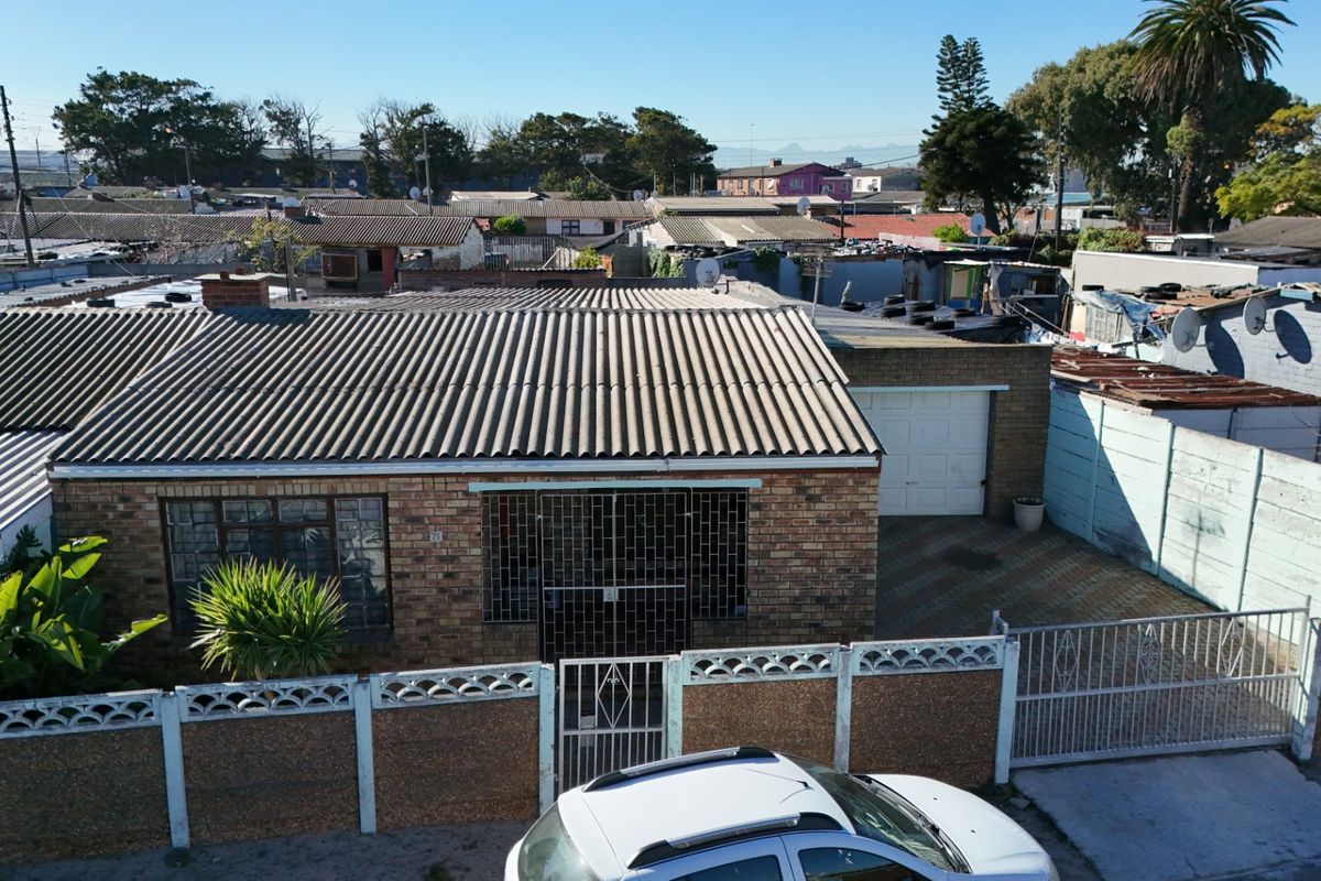 Aerial view of a single-story brick house featuring a corrugated roof, attached garage, paved driveway, and secure boundary walling in a residential neighborhood.