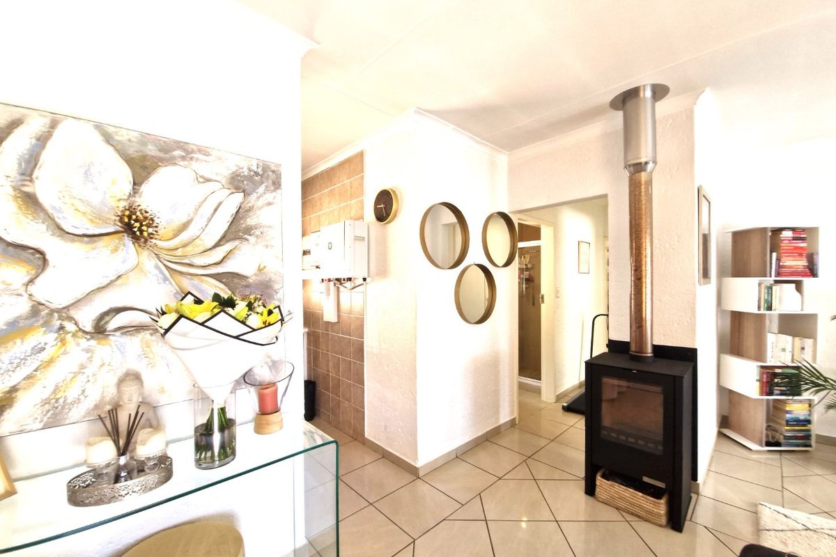 Living area featuring tiled flooring and a modern freestanding fireplace, with an adjacent hallway leading to utility space.
