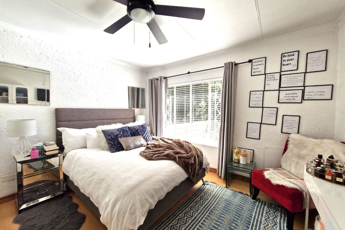 A well-lit bedroom featuring textured walls, a ceiling fan, and large windows with venetian blinds, providing a comfortable and functional living space.