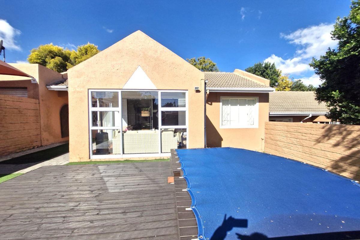 Rear exterior view of the townhouse featuring a swimming pool with a cover, timber decking, and large sliding glass doors leading into the home.