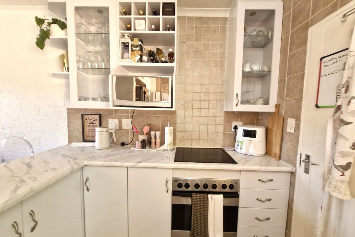 A functional kitchen featuring white cabinetry, marble-look countertops, a ceramic tile backsplash, and integrated cooking appliances including an electric hob and oven.