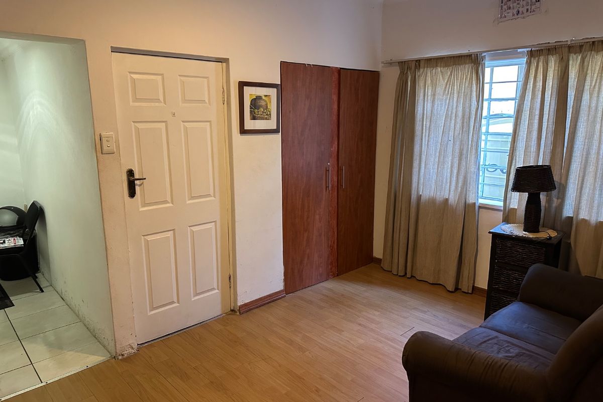 A bedroom featuring laminate flooring, a built-in wardrobe, and security bars on the window, offering a functional space with potential for cosmetic updates.