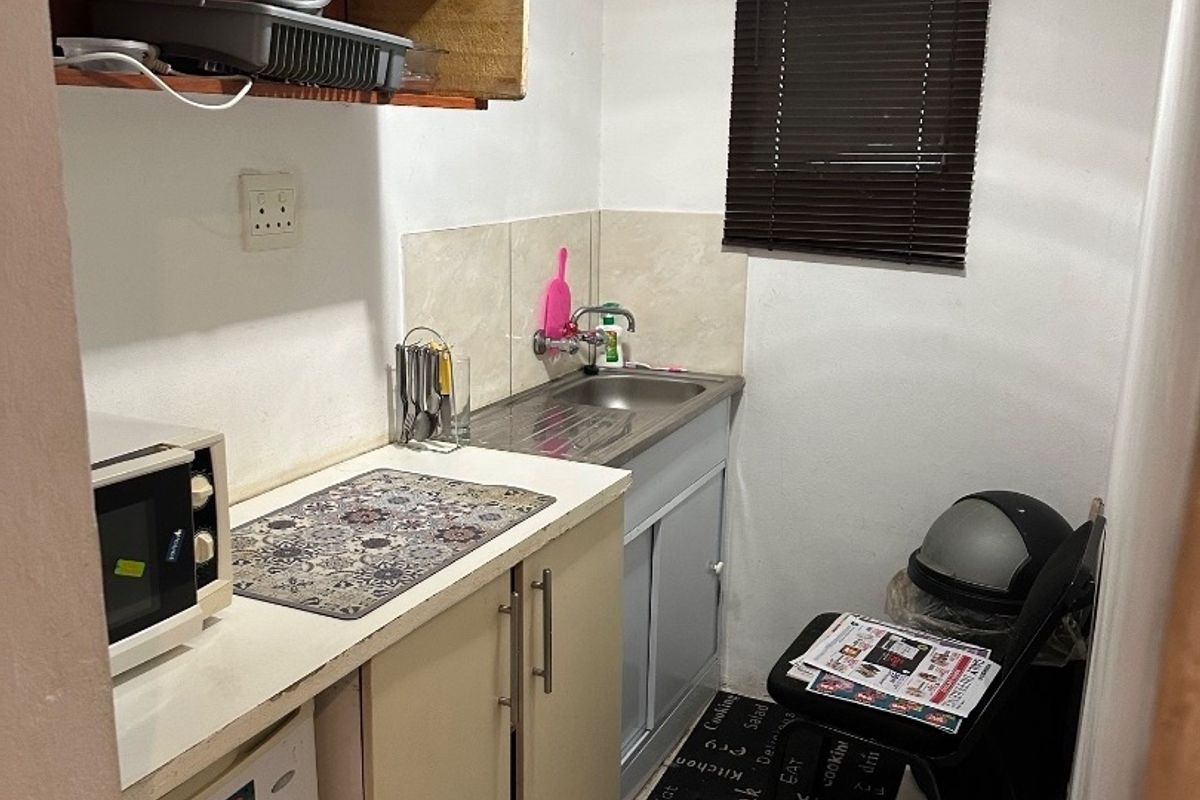 A compact scullery area featuring built-in cabinetry, a stainless steel sink, and tiled splashbacks, offering functional utility space for food preparation and cleaning.