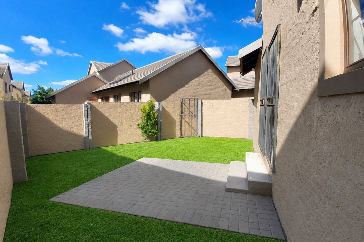 A well-maintained rear garden featuring a paved patio area, artificial lawn, and secure boundary walls, providing a private outdoor space.