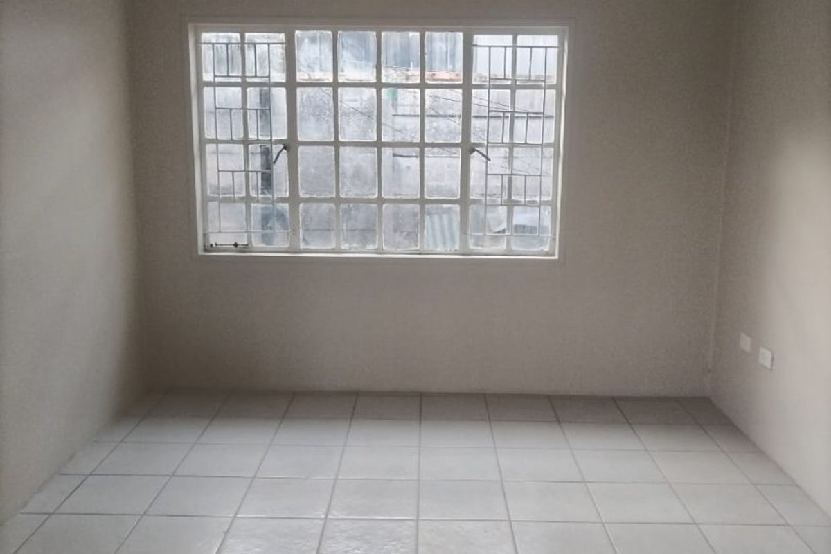 A clean, empty bedroom featuring neutral tiled flooring, recessed downlighting, and a window fitted with security bars.