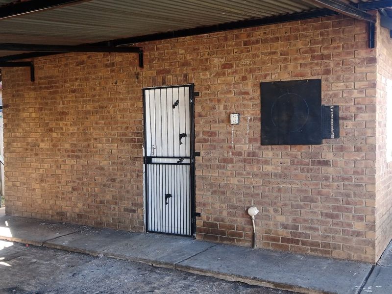 Rear exterior view of a face brick structure featuring a security gate, corrugated metal roof, and concrete apron.