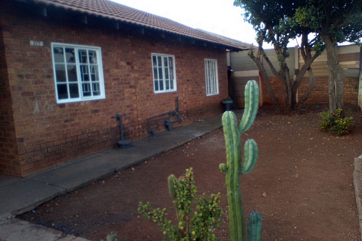 Rear view of a face brick house featuring a tiled roof, concrete pathway, and a garden area with established trees.