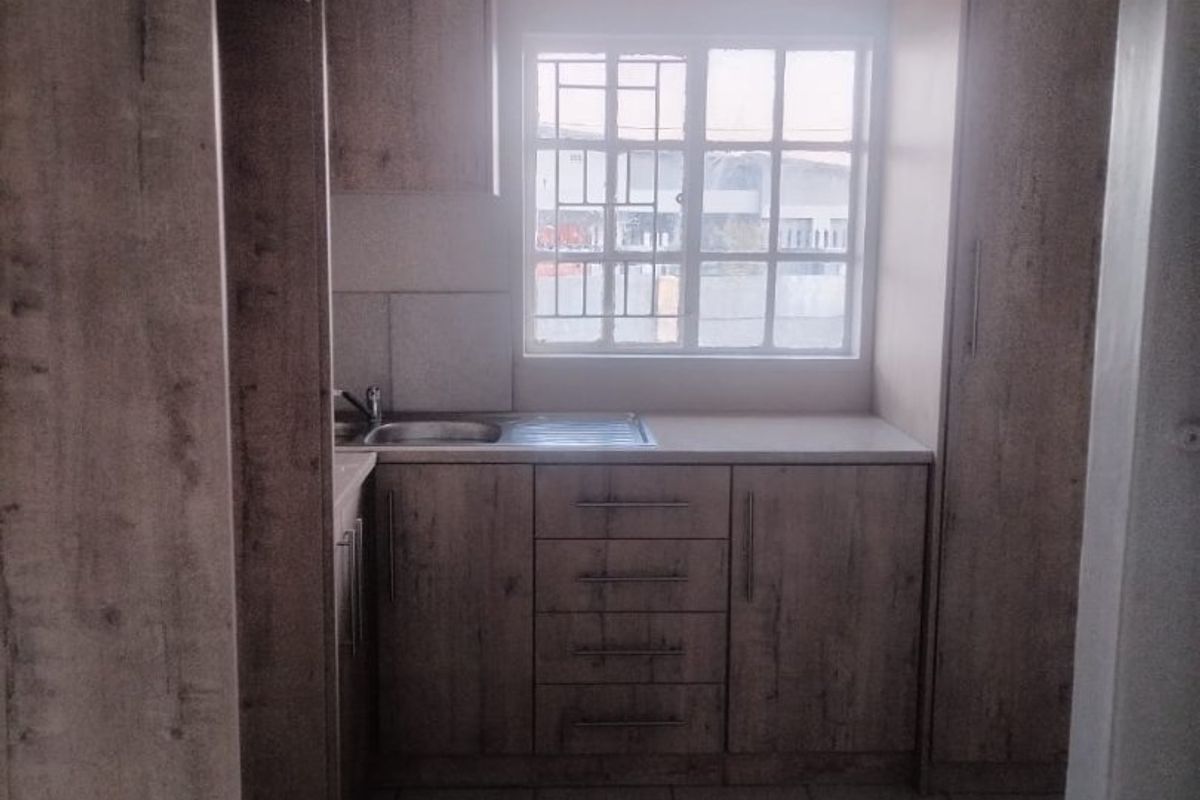 A compact kitchen featuring wood-look cabinetry, tiled flooring, and a functional sink area with natural light from a window.