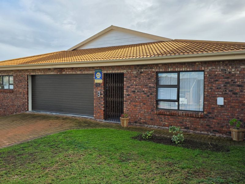 Front elevation of a face brick house featuring a tiled roof, automated garage door, and paved driveway with a small front garden.