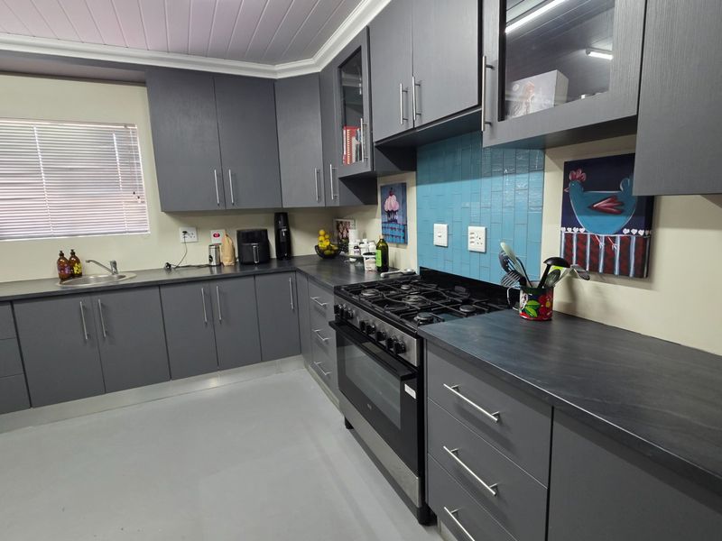 A functional kitchen featuring modern grey cabinetry, dark laminate countertops, a gas stove with extractor, and a tiled splashback.