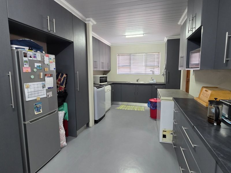 A functional kitchen featuring dark grey cabinetry, laminate countertops, a stainless steel sink, and a clean, neutral aesthetic with tongue and groove ceiling detailing.