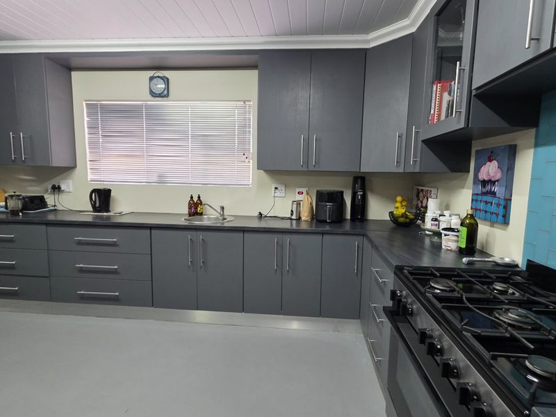 Modern kitchen featuring grey cabinetry, dark laminate countertops, a gas cooktop, and a vibrant blue tiled splashback.
