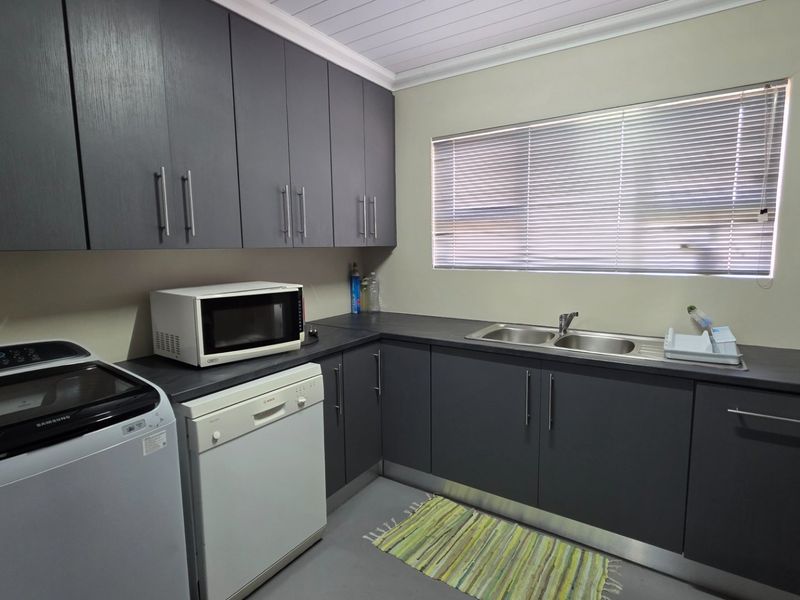 A functional laundry room featuring dark grey built-in cabinetry, a double bowl sink, and a clean, modern aesthetic with ample storage space.