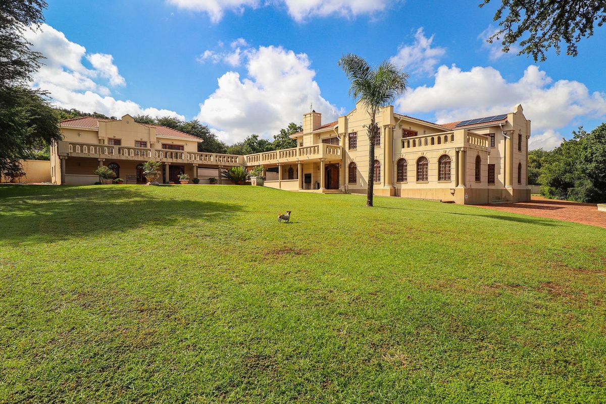 Spacious rear view of a large multi-story residence featuring expansive lawn, upper-level balconies, classic architectural columns, and a decorative garden fountain.