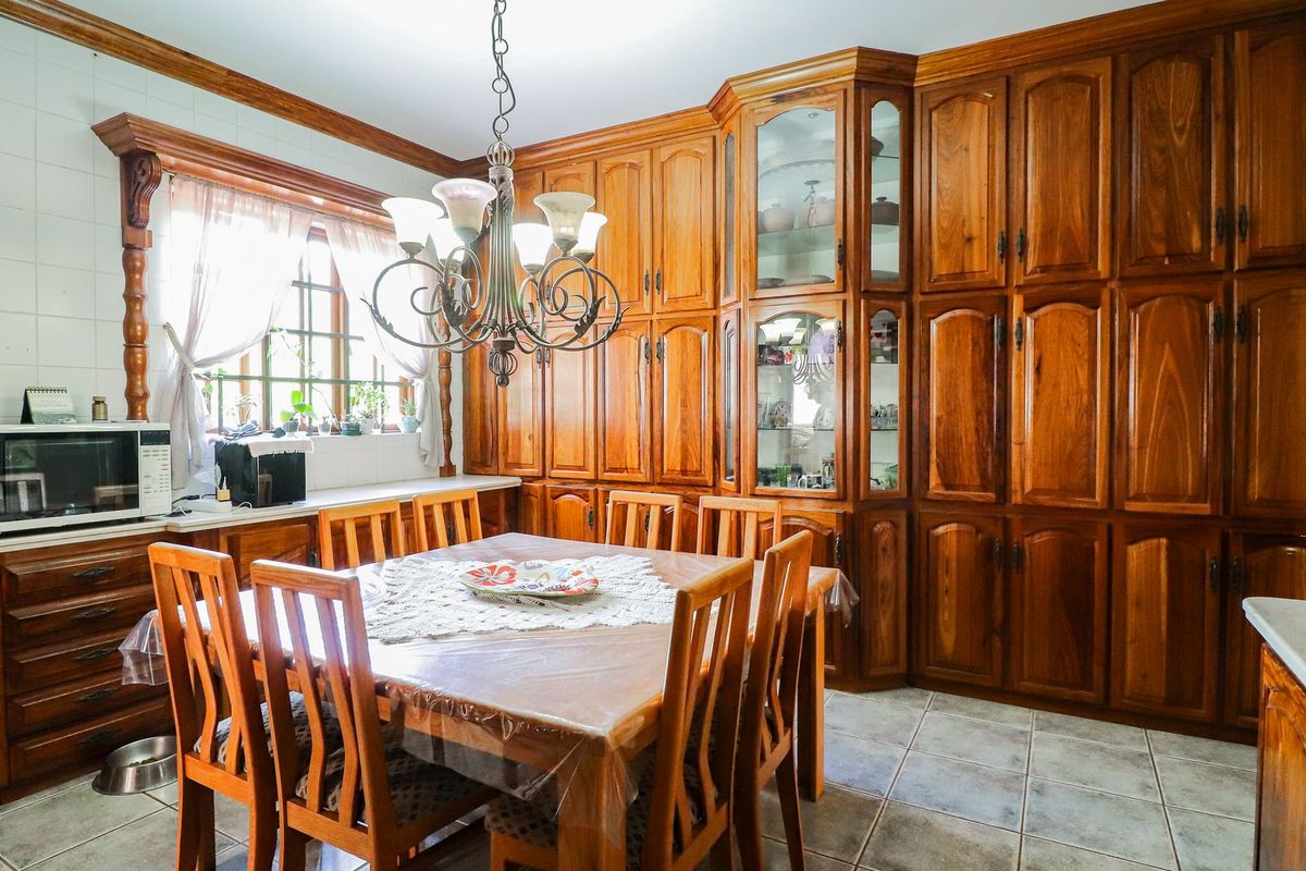 A traditional kitchen featuring extensive built-in timber cabinetry, tiled flooring, and a dedicated dining area with a classic chandelier.