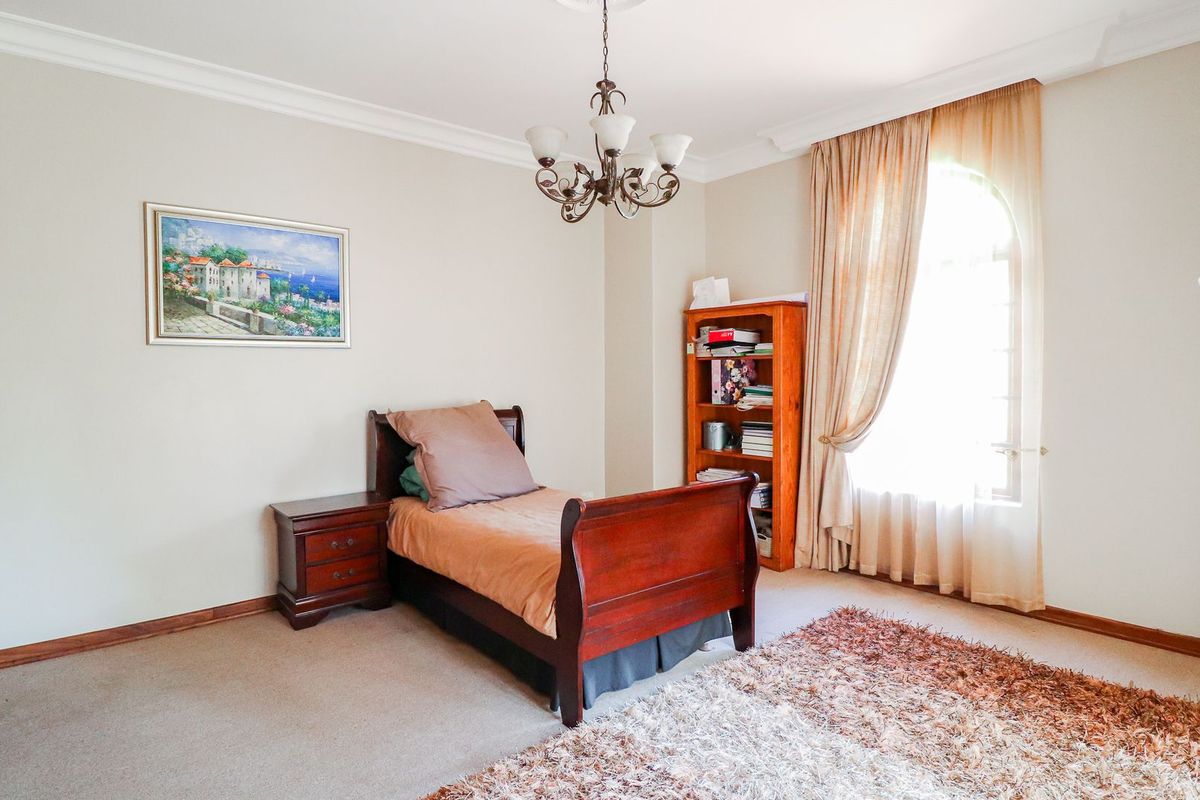 A well-proportioned bedroom featuring neutral walls, coving, an arched window with curtains, and a built-in wardrobe.